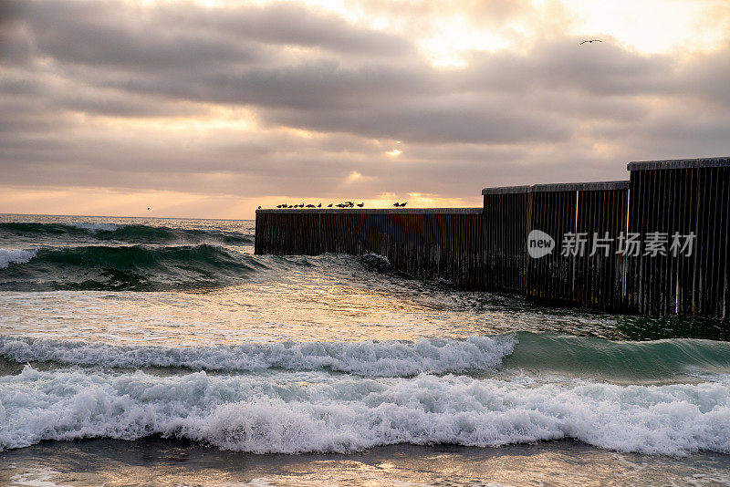 海滩和海浪的近景日落附近的国际边界墙在Playas Tijuana，墨西哥